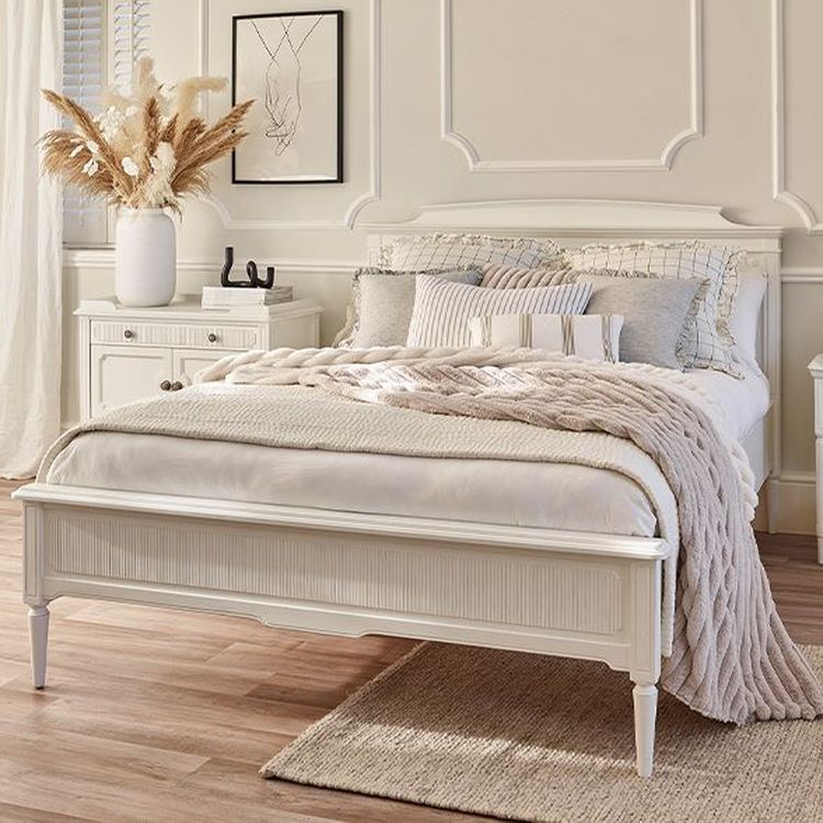 Elegant bedroom with a white bed, beige knitted throw, textured pillows, nightstand, pampas grass in a vase, and soft natural lighting.