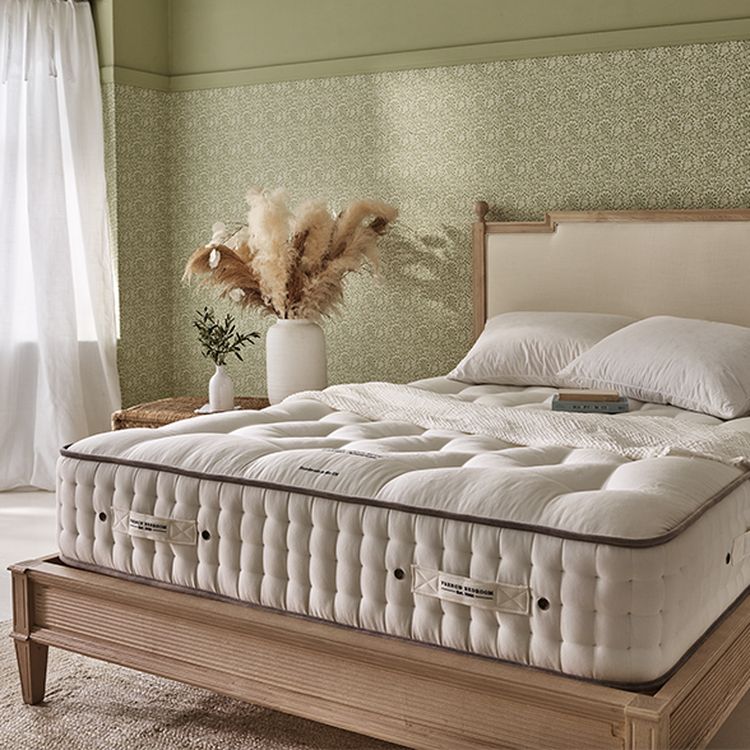 Cozy bedroom with a plush mattress on a wooden bed frame, white bedding, a vase with pampas grass, and soft natural light from a window.