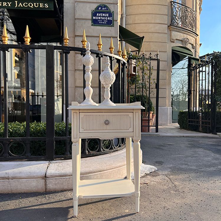 Elegant white side table with ornate candlesticks on top, placed on a sidewalk near a wrought iron fence and a building with a balcony.