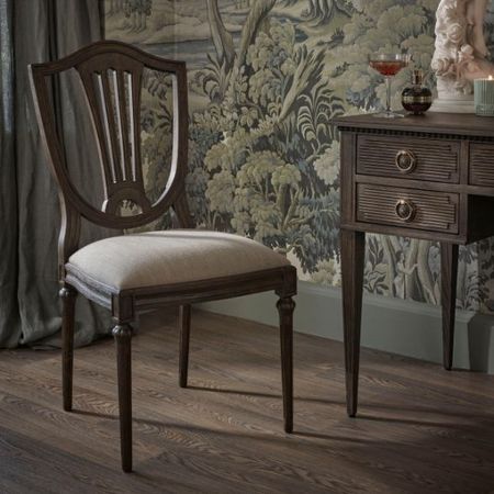 Elegant wooden chair with cushioned seat beside a vintage desk, set against a detailed, nature-themed wallpaper and wooden floor.