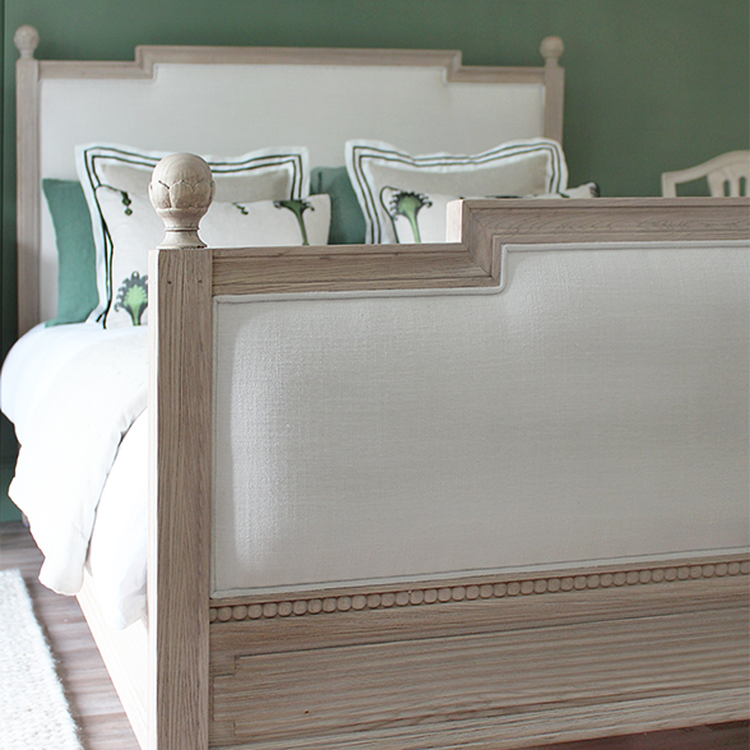Wooden bed with white upholstered headboard and footboard, adorned with green and white pillows, set against a green wall.