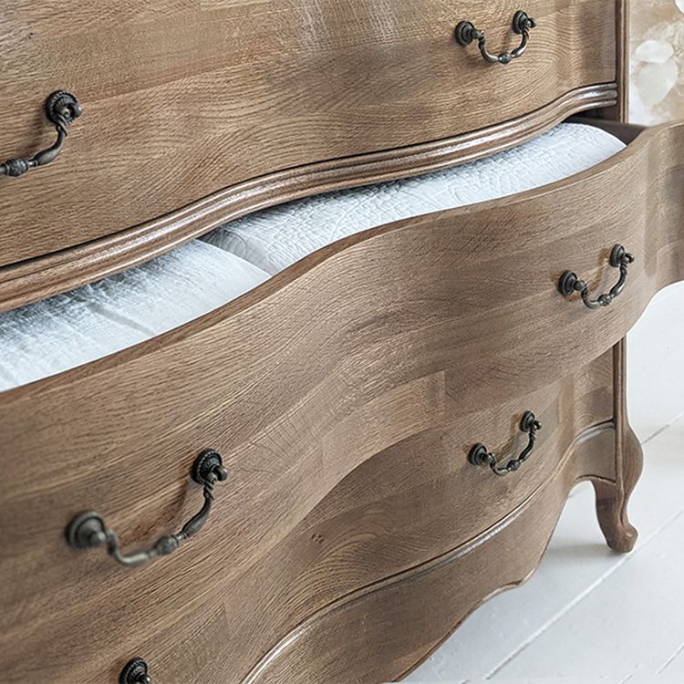 Wooden dresser with ornate handles and two open drawers revealing neatly folded white linens inside.