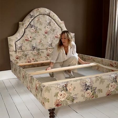 Woman assembling a floral-patterned bed frame in a room with dark walls and white wooden flooring.