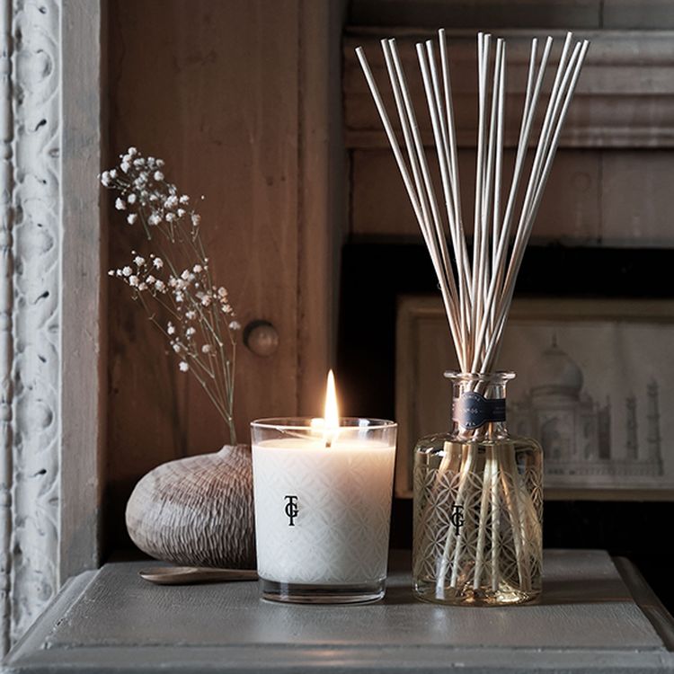 Lit candle and reed diffuser on a table, with decorative stones and baby's breath flowers, creating a cozy ambiance.