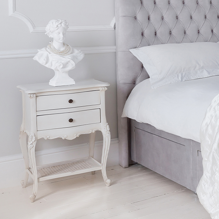 Elegant bedroom scene with a tufted headboard, white bedding, and a vintage nightstand featuring a classical bust sculpture.