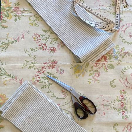 Fabric pieces, a measuring tape, and scissors on a floral-patterned surface, suggesting a sewing or crafting project.