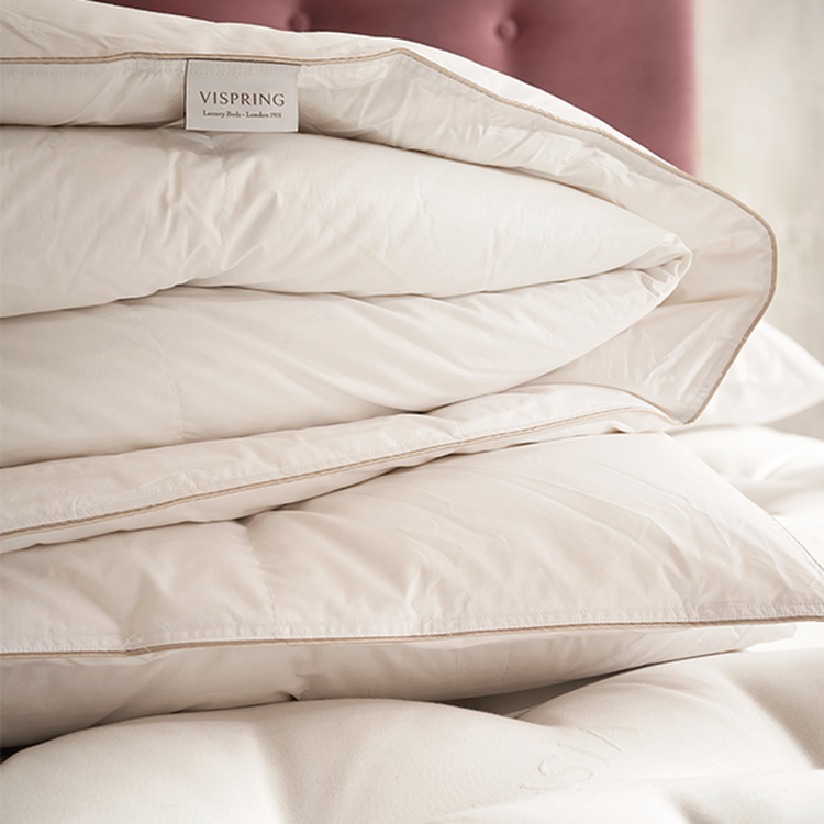 Close-up of a neatly folded, luxurious white duvet with a visible Vispring label, set against a soft pink headboard.