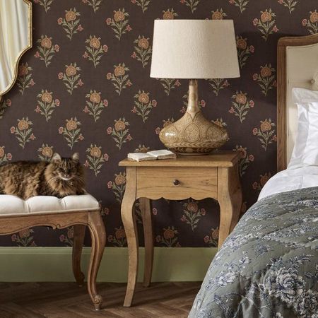Single drawer bedside table with minimal styling including a lamp and an open book, beside an upholstered bed.