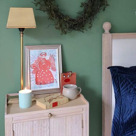 Pale wood bedside with bronzed gold lamp and a collection of personal items on top.