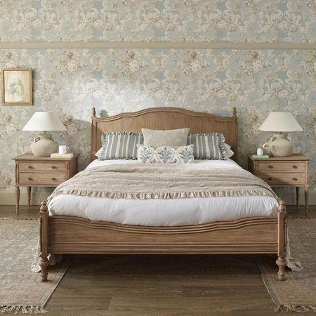 Solid wooden carved French bed with pale cream, beige, and blue styling. Two matching wooden bedsides with matching large beige lamps upon them. a hotel inspired bedroom styling.
