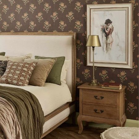 Short 2 drawer bedside table with a brass lamp placed on top and wall art behind.