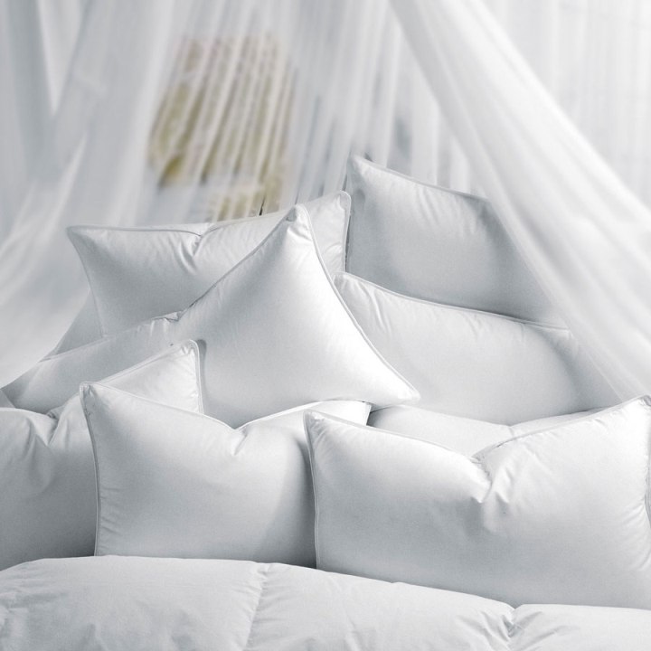 A pile of fluffy white pillows arranged on a bed, surrounded by sheer white curtains, creating a soft and cozy atmosphere.