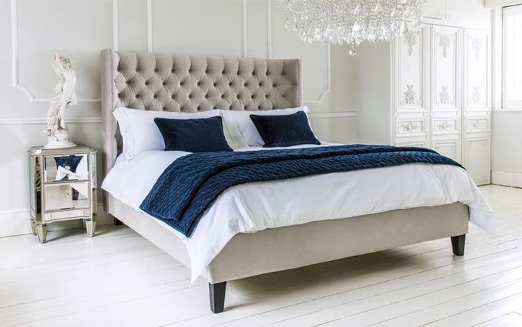 Elegant bedroom with a tufted headboard bed, white bedding, and navy accents. A mirrored nightstand and chandelier add luxury.
