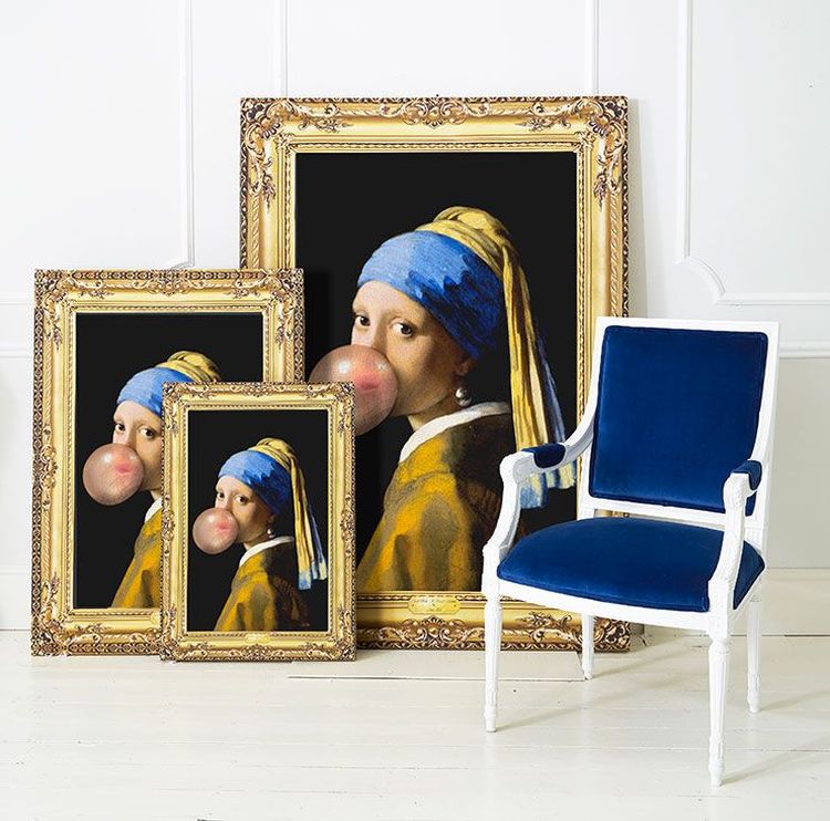 Three framed prints of "Girl with a Pearl Earring" blowing bubblegum, next to a blue velvet chair, against a white wall.