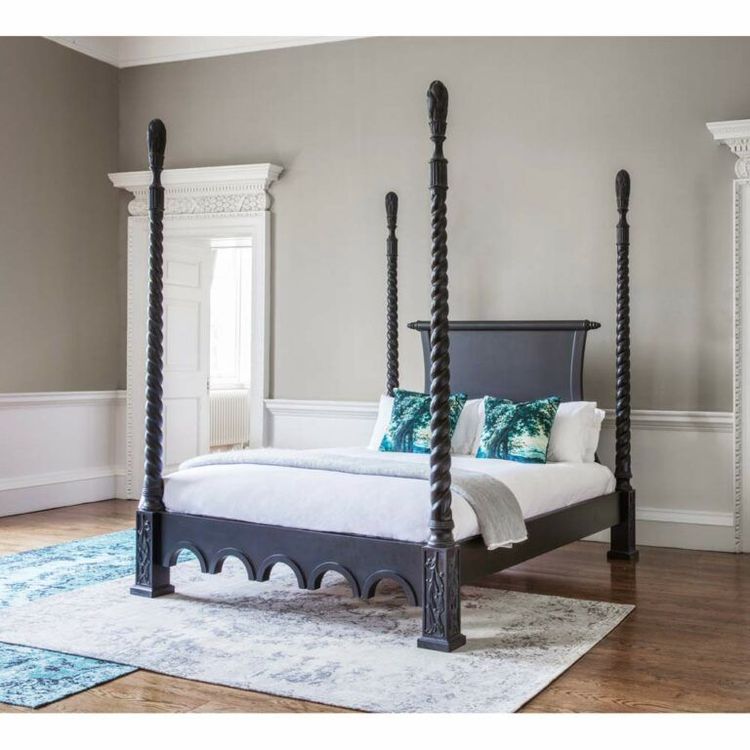 Elegant four-poster bed with twisted black posts, white bedding, and teal pillows in a spacious room with gray walls and wooden floor.