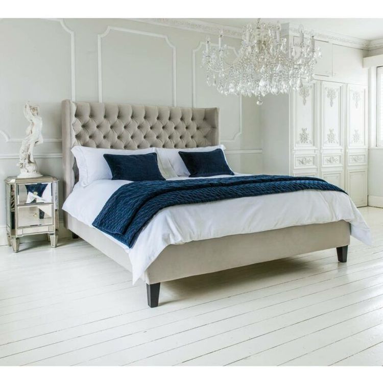 Elegant bedroom with a tufted headboard bed, navy pillows, white bedding, chandelier, and ornate white walls and furniture.