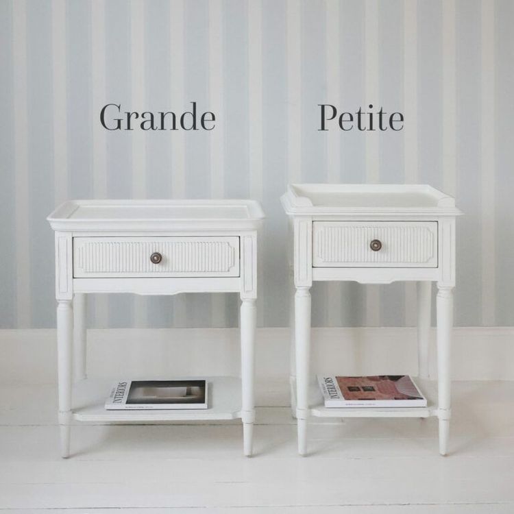 Two white side tables labeled "Grande" and "Petite" against a striped wall. Each has a drawer and a magazine on the lower shelf.