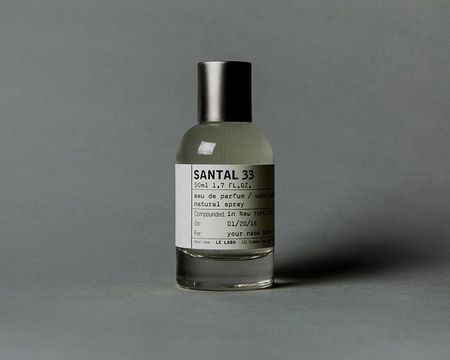 A bottle of Santal 33 perfume with a silver cap and minimalist label, set against a neutral background.