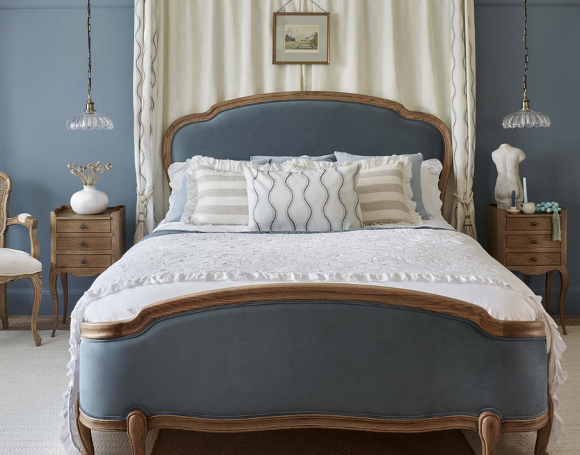 Elegant bedroom with a blue upholstered bed, decorative pillows, wooden nightstands, and pendant lights, creating a serene and classic atmosphere.