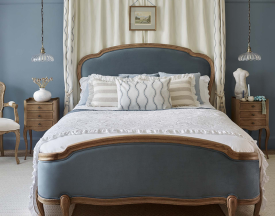 Elegant bedroom with a blue upholstered bed, decorative pillows, wooden nightstands, and pendant lights, creating a serene and classic atmosphere.