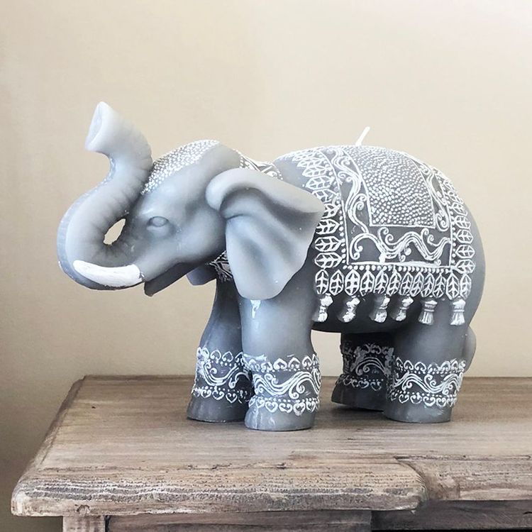 Gray elephant figurine with intricate white patterns stands on a wooden surface against a beige background.
