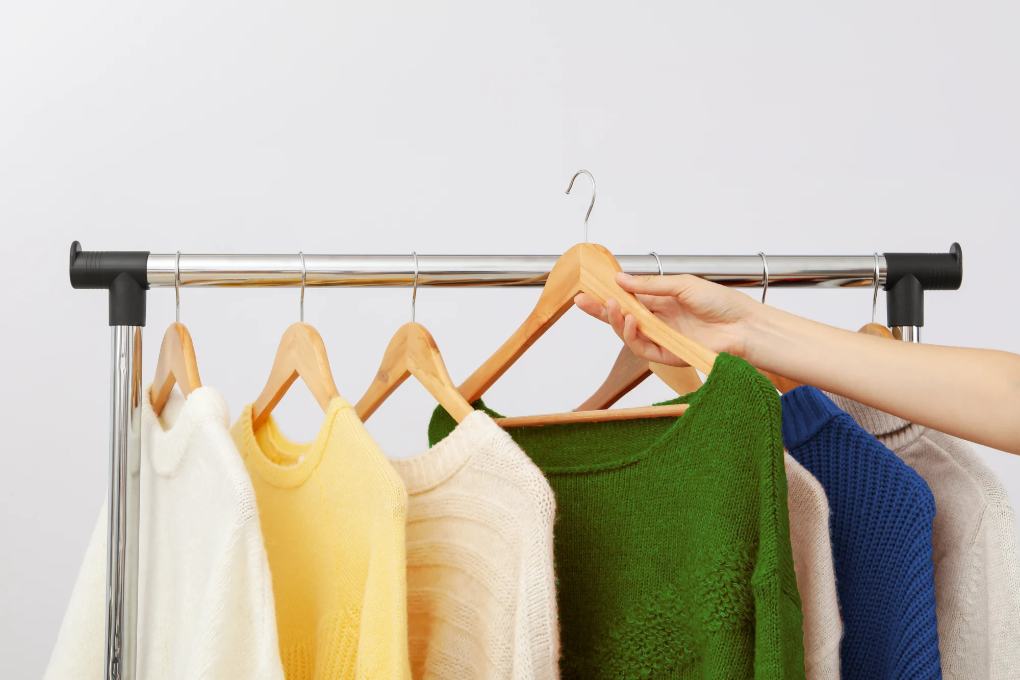 A hand selects a green sweater from a row of colorful sweaters