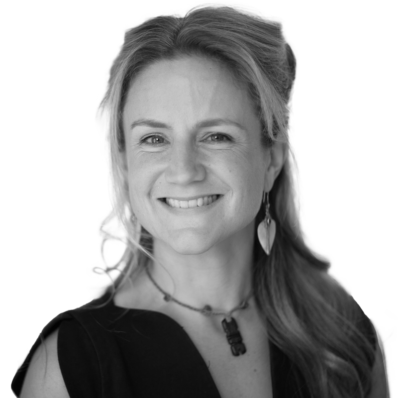 Smiling woman with long hair, wearing a necklace and leaf-shaped earrings, in a black and white portrait.