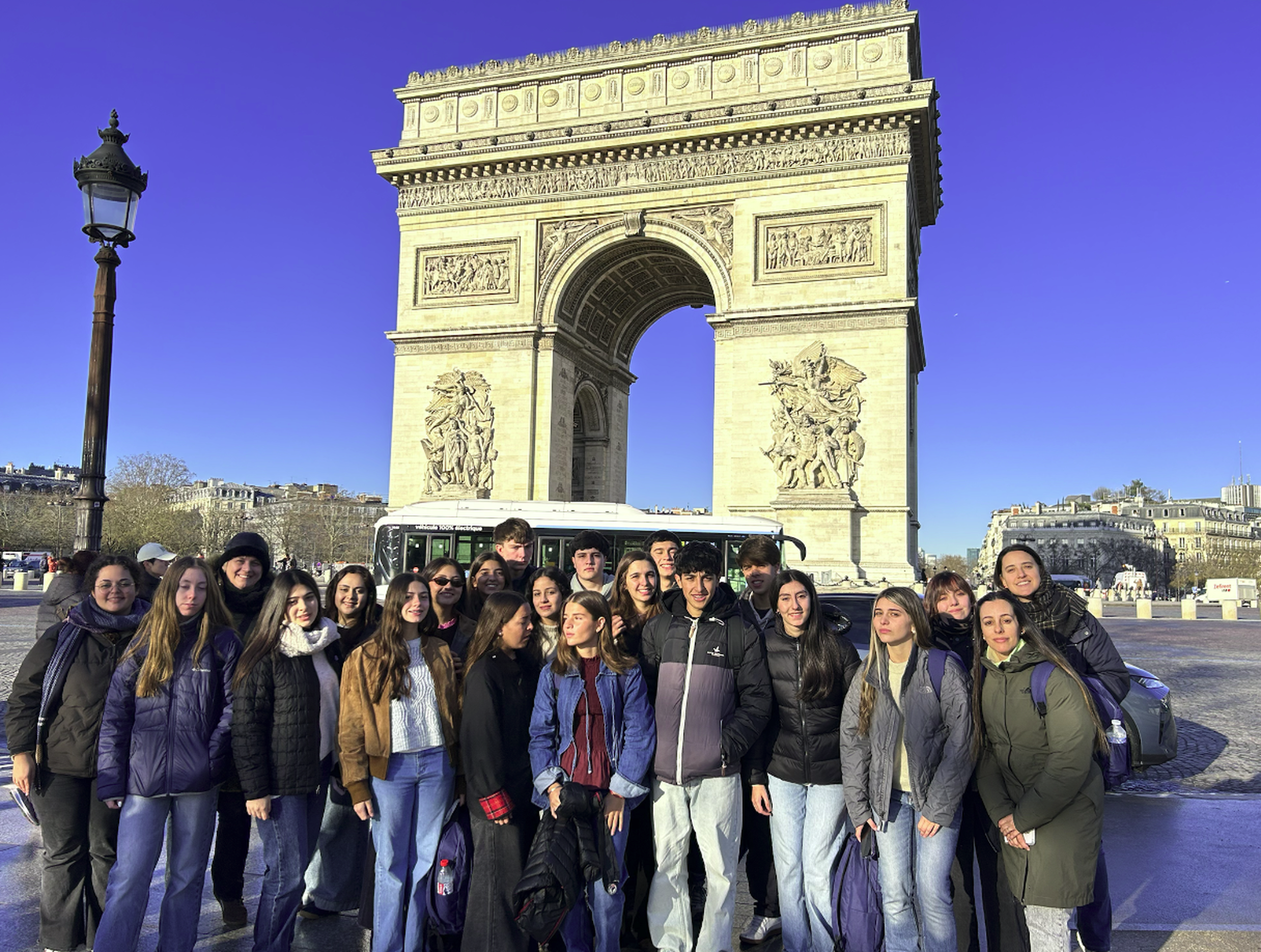 Grupo de estudiantes en viaje de estudios frente al Arco de Triunfo en París durante excursión educativa en Europa