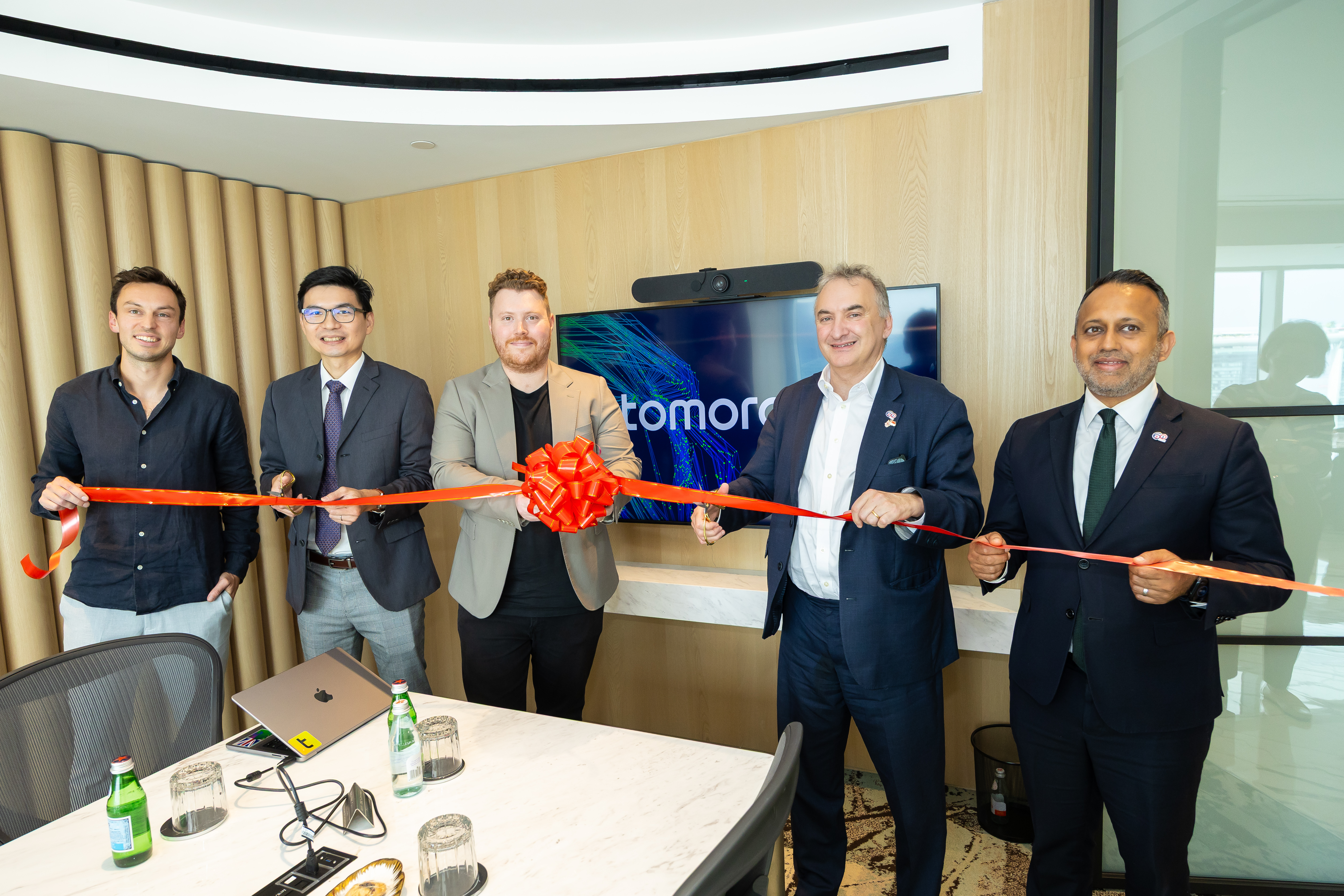 Five men in business attire stand together cutting a red ribbon in a modern conference room, celebrating an event.