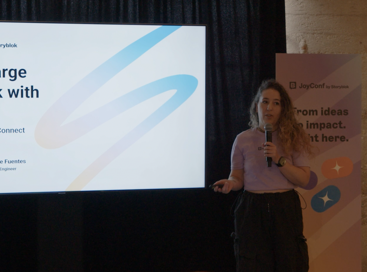 A person presenting at JoyConf by Storyblok, standing next to a screen displaying a presentation.