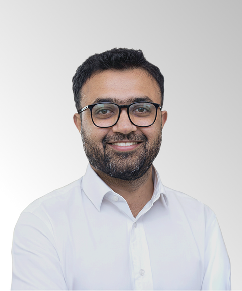 Smiling man with glasses and beard, wearing a white shirt, against a gray gradient background.