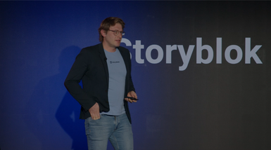 A person in a blazer and jeans speaks on stage in front of a large "Storyblok" logo.
