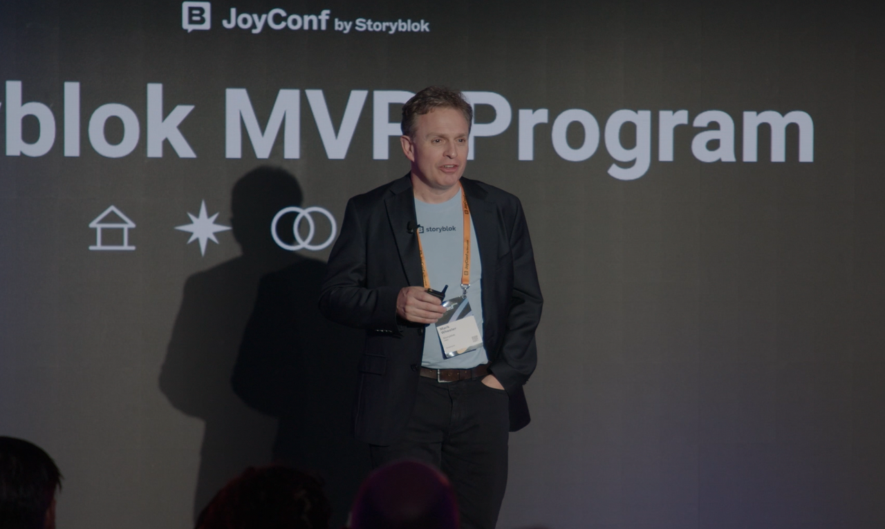 A person speaking on stage at JoyConf by Storyblok, with "blok MVP Program" displayed on the screen behind.