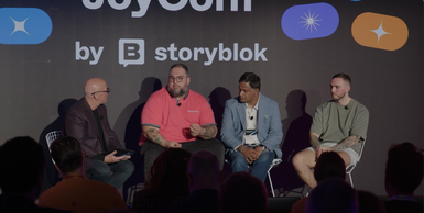 Four men seated on stage for a panel discussion at a conference, with a "by storyblok" banner in the background.