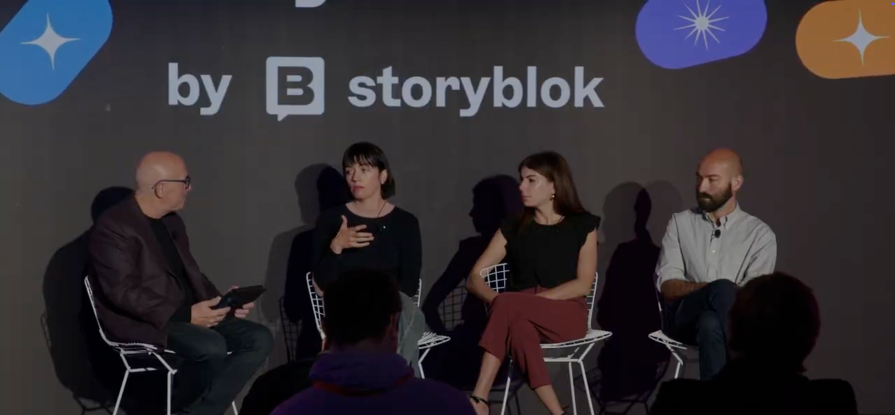 Four people seated on stage during a panel discussion, with a backdrop displaying "by storyblok" and colorful icons.