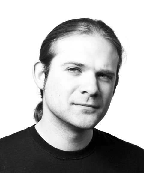 Black and white portrait of a person with long hair tied back, wearing a dark shirt.