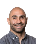 A smiling man with a shaved head, wearing a gray button-up shirt, against a plain background.