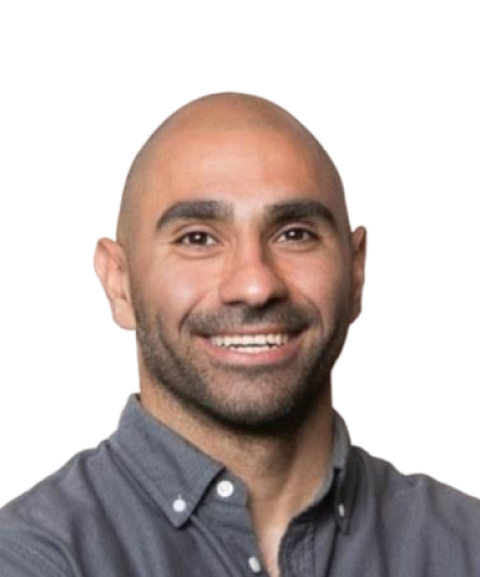 A smiling man with a shaved head, wearing a gray button-up shirt, against a plain background.