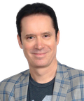 Smiling man with dark hair wearing a plaid blazer and a dark t-shirt, looking directly at the camera.