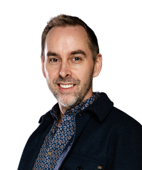 A smiling man with short hair, wearing a patterned shirt and dark jacket, looking towards the camera against a plain white background.