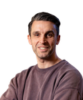 Smiling man with short dark hair and a beard, wearing a brown sweatshirt, posing against a plain white background.