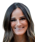 Smiling woman with long, wavy brown hair and a natural look, facing the camera against a white background.