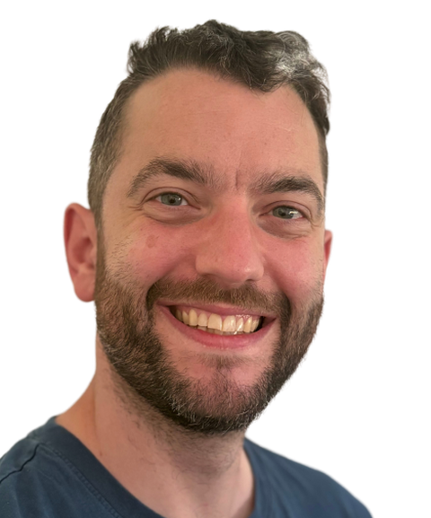 Smiling man with short dark hair and a beard, wearing a dark shirt against a plain background.