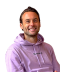 Smiling man in a lavender hoodie, sitting and looking forward.