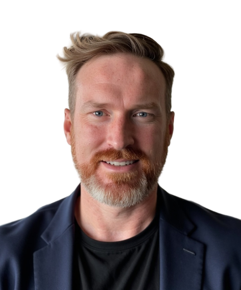 A man with a red beard and styled hair wearing a dark blazer, smiling against a white background.