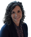 Smiling woman with curly hair wearing a patterned blouse and blazer.