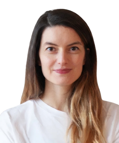Woman with long brown hair wearing a white shirt, smiling at the camera against a plain background.