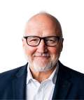 Bald man with glasses and a beard, wearing a dark blazer and white shirt, smiling slightly against a plain background.