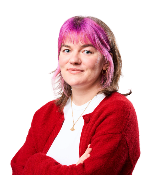 Person with pink hair wearing a red cardigan, smiling with arms crossed against a white background.