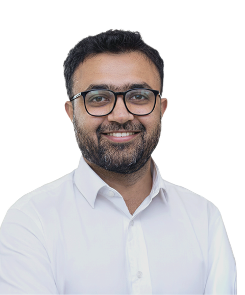 A smiling man with glasses and a beard, wearing a white shirt, stands against a plain background.